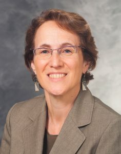 A woman with short brown hair wearing glasses and a tan blazer
