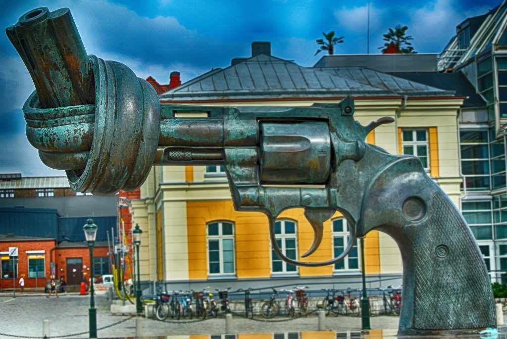 A photo of a bronze sculpture. It depicts a gun with the end tied in order for the gun not to fire. 