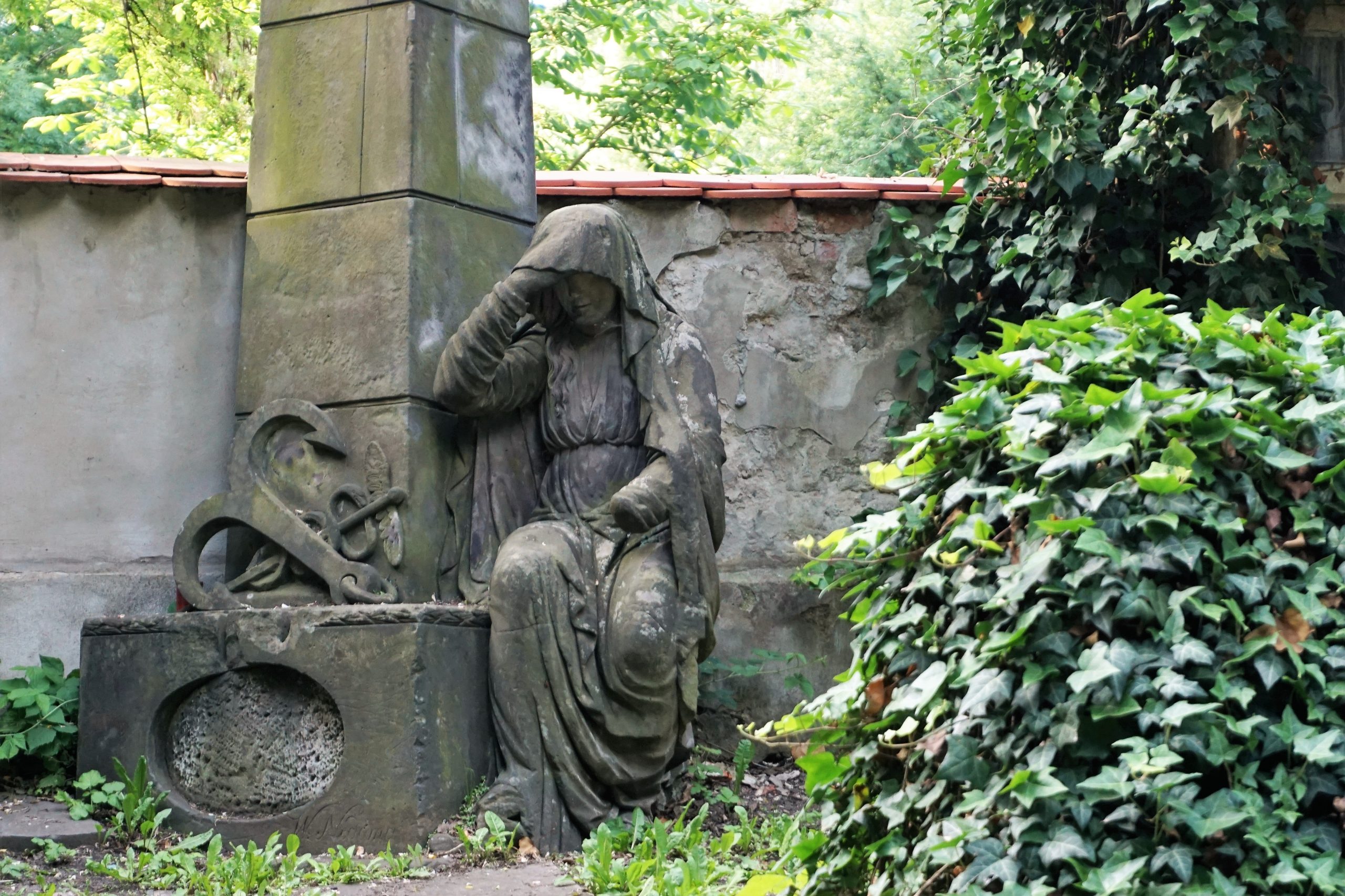 This image depicts a neoclassical statue found within the Olšany Cemetery in Prague.