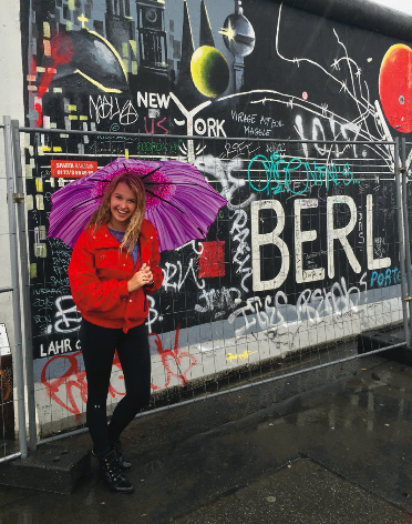image of study abroad alumna Emily Menting in front of a remaining section of the Berlin Wall, in Berlin, Germany.